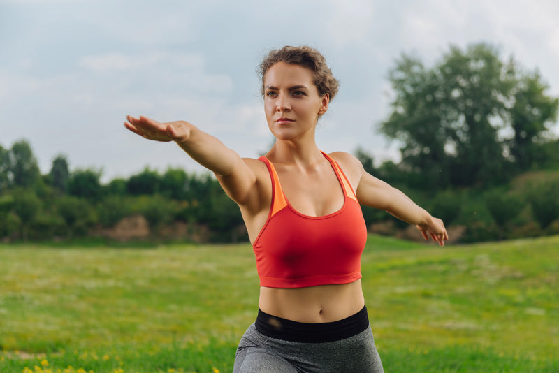 Frau steht in Yoga-Pose auf einer Wiese