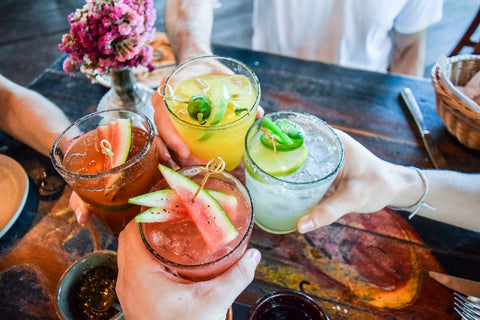 Eine Gruppe Freundinnen und Freunde stößt mit vier bunten Cocktails an