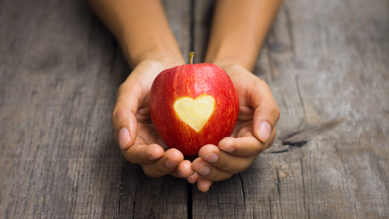 Zwei Hände halten einen Apfel, in den ein Herz geschnitten ist