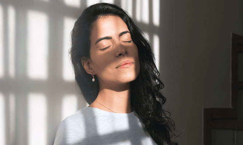 Vitamin D Bildung unter der Haut: Eine Frau genießt Sonnenstrahlen und schaut mit geschlossenen Augen Richtung Sonne