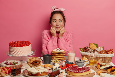 Frau sitzt vor vielen verschiedenen Kuchen und Gebäcken