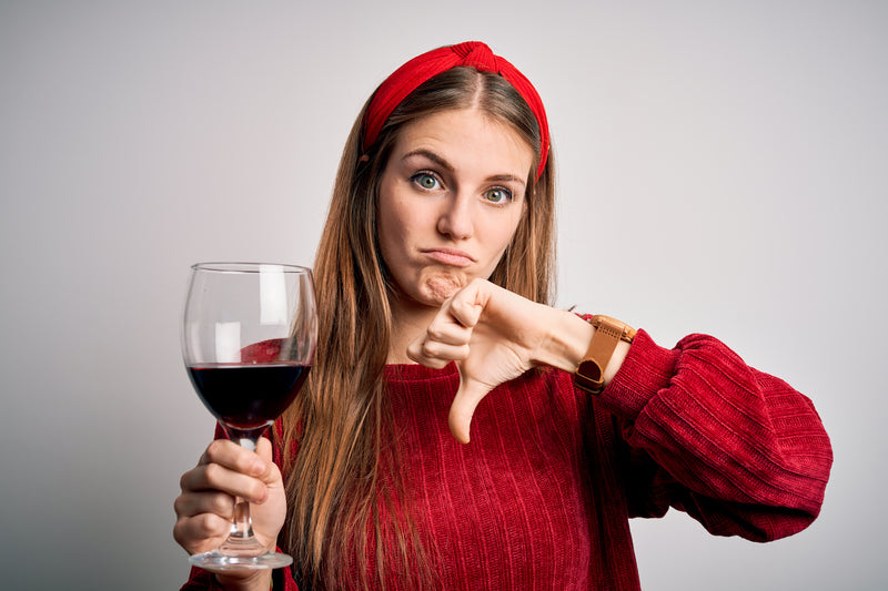 Frau mit einem Weinglas zeigt mit dem Daumen nach unten