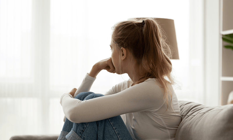 Frau sitzt auf dem Sofa und leidet unter den Symptomen ihres Progesteronmangels