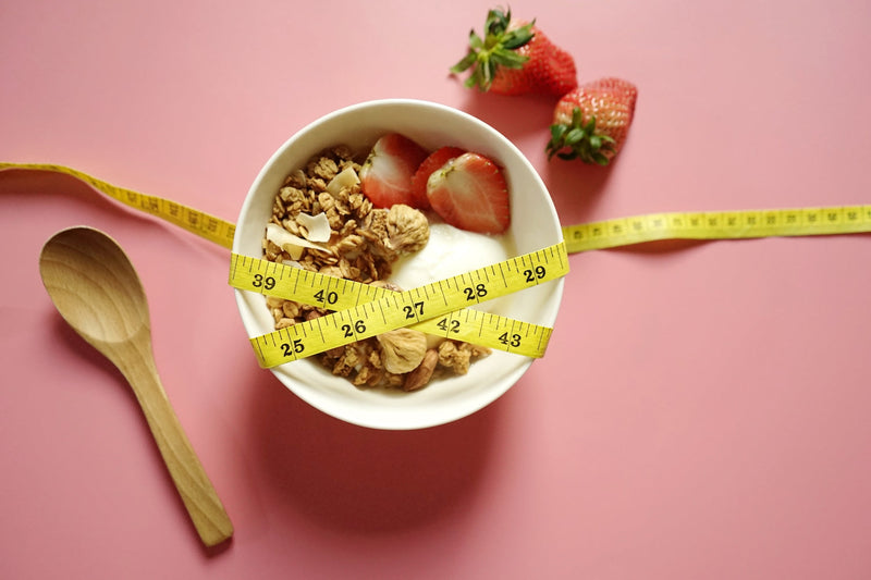 Schüssel mit Müsli und Obst, darum ein Maßband