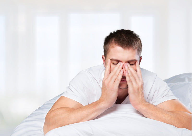Mann liegt auf dem Bett und reibt sich müde die Augen