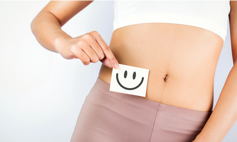 Frau hält einen gezeichneten, lachenden Smiley vor ihren Bauch