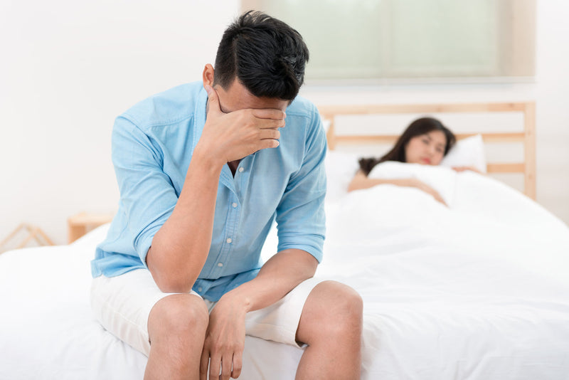 Mann sitzt auf dem Bett und stützt den Kopf auf die Hand