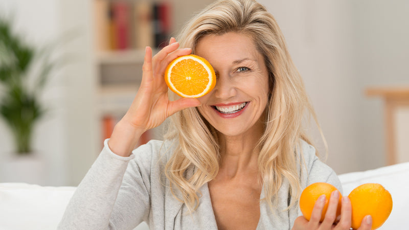 Wechseljahre Symptome, Maßnahmen, Tipps: Frau hält sich halbe Orange vors Gesicht 