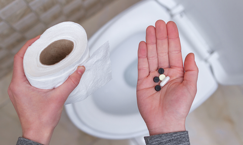 Person hält Toilettenrolle und Abführmittel in Kapselform in der hand