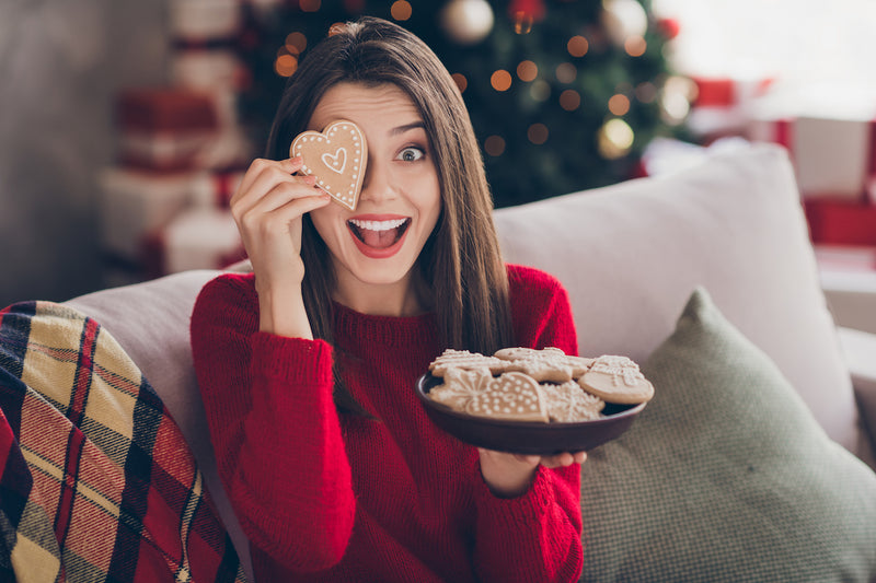 Frau hält sich einen Weihnachtskeks in Herzform vor ein Auge