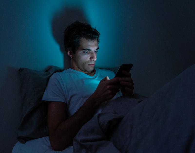 Mann sitzt nachts mit Handy im Bett