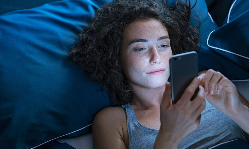 Eine junge Frau ist spät im Bett liegend noch am Handy