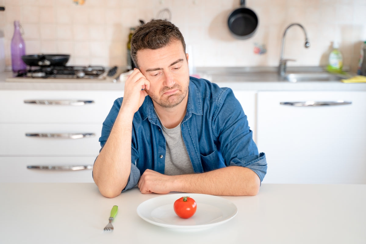 Mann sitzt vor Teller mit einer Tomate