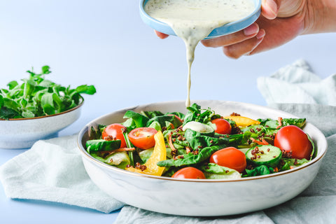 Jemand kippt ein Dressing über einen bunten Salat