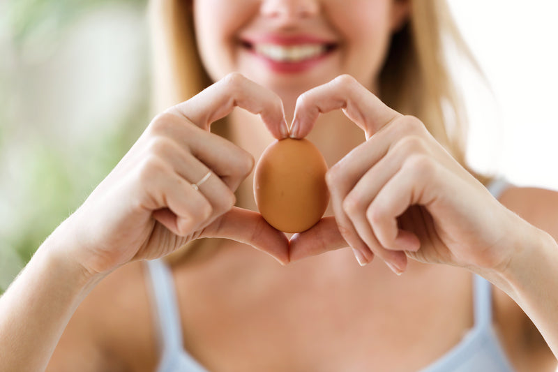 Frau macht Herz mit Fingern und hält dabei ein Ei