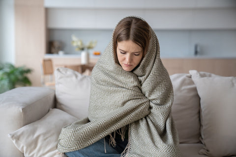 Eine Frau sitzt erkältet in Decken gehüllt auf der Couch