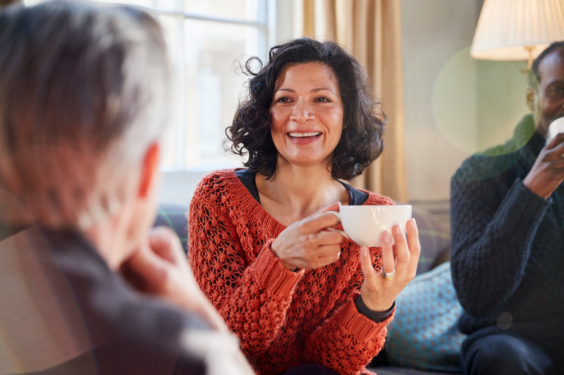 Eine Frau sitzt mit Kaffee in der Hand und Freunden im Café