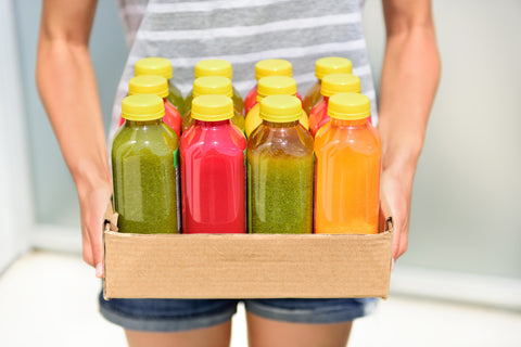 Ein Mann hält in einem Karton viele verschiedene Fruchtsäfte und Smoothies