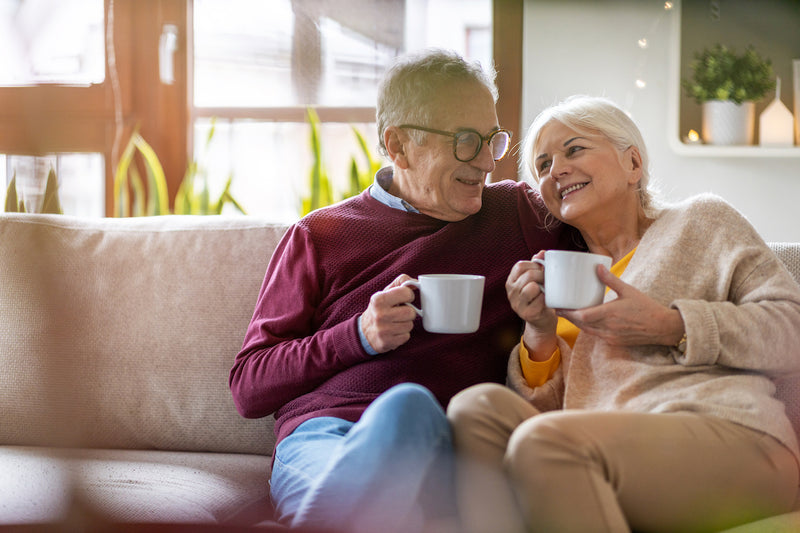Älteres Paar sitzt mit Kaffeetassen auf dem Sofa
