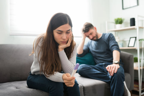 Ein junges Paar sitzt verzweifelt auf der Couch und schaut bedrückt auf einen negativen Schwangerschaftstest