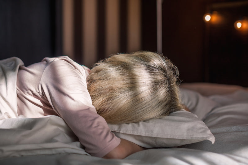 Eine Frau liegt mit Gesicht im Kissen vergraben im Bett