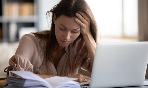 Eine junge Frau sitzt sehr müde auf der Arbeit vor dem Laptop