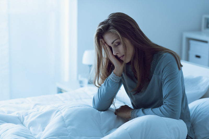 Frau sitzt müde aufrecht im Bett aufgrund eines Calciummangels