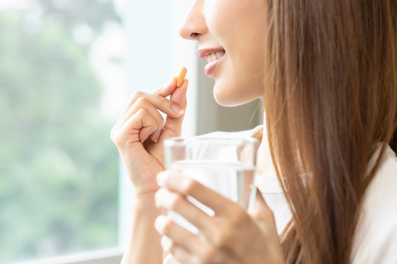 Frau nimmt Kapsel mit einem Glas Wasser ein