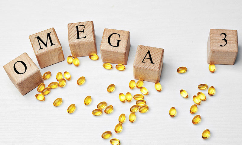 Nährstoffe in der Schwangerschaft: Holzklötze mit der Aufschrift OMEGA 3, darum Kapseln mit Omega-3-Fettsäuren