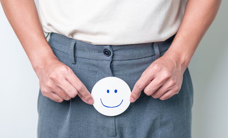 Ein Mann hält einen grinsen Smiley aus Papier vor seine Hose