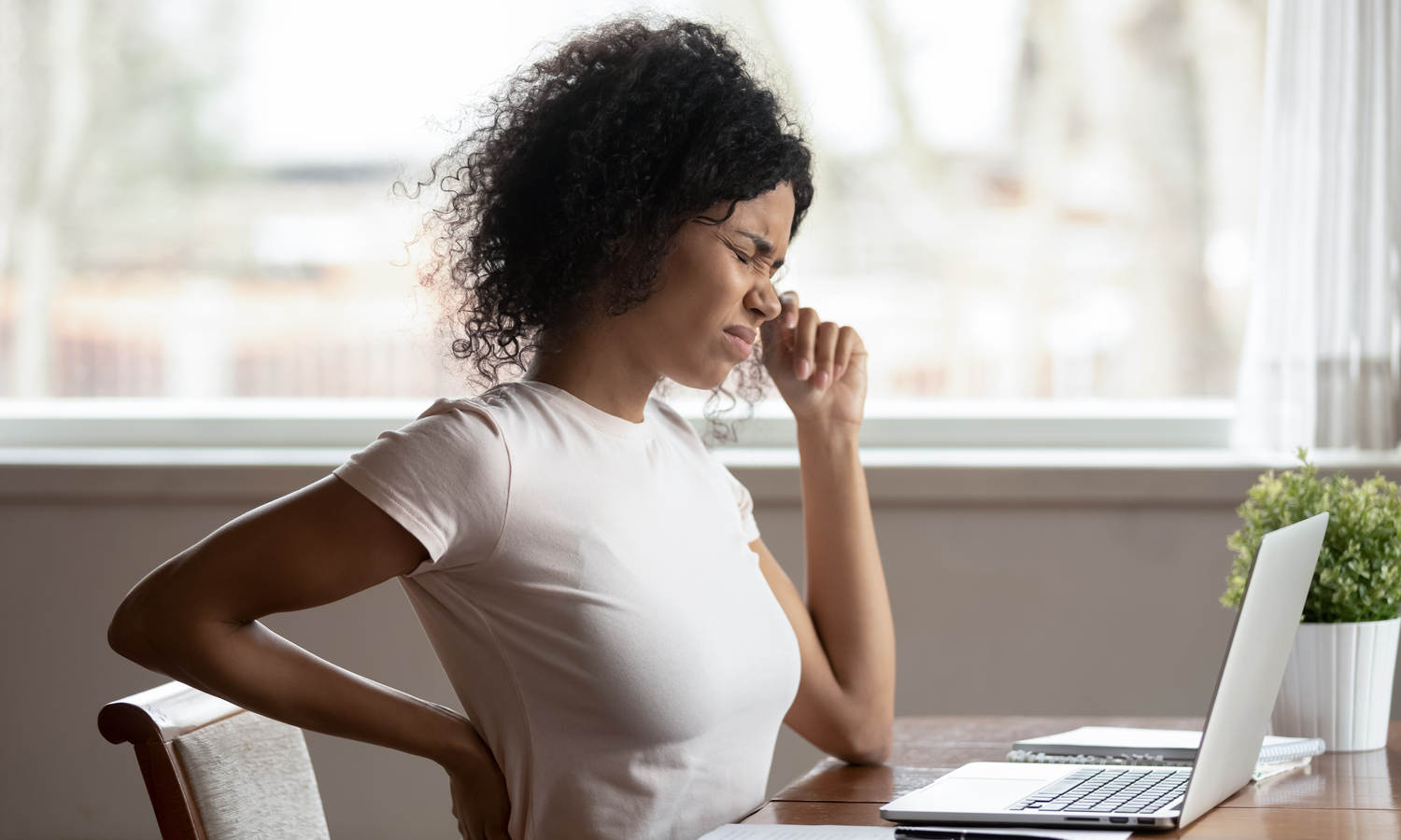 Frau am Schreibtisch hält sich vor Schmerz die Hand an den Rücken