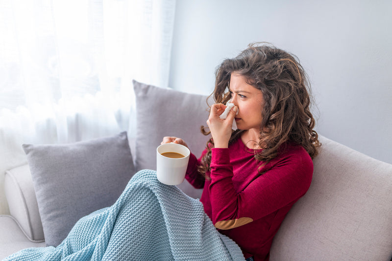 Frau sitzt mit einer Erkältung auf dem Sofa