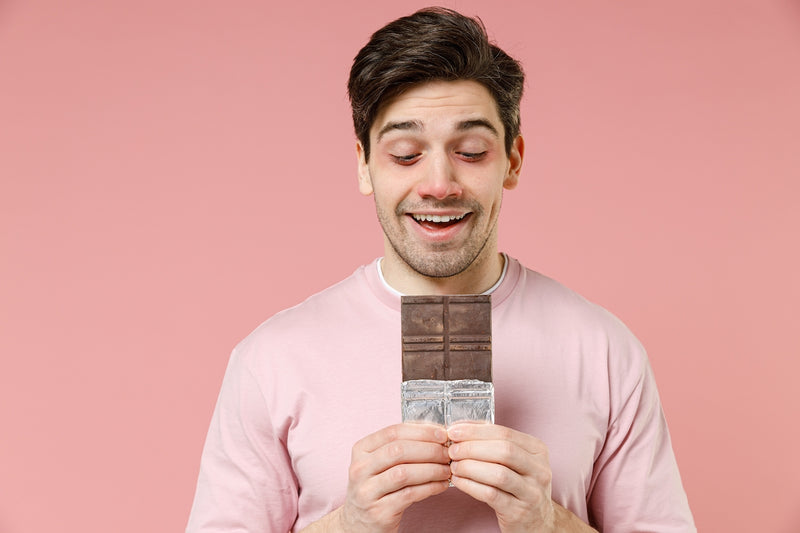 Mann hält freudig eine Tafel Schokolade in der Hand