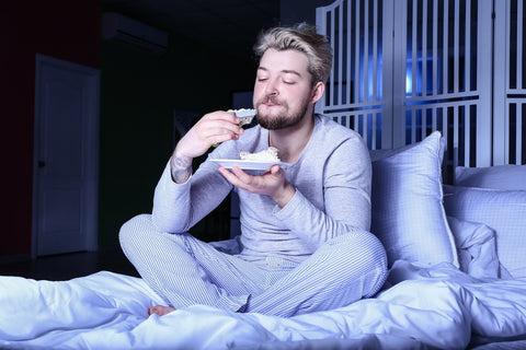 Mann isst Snacks im Bett