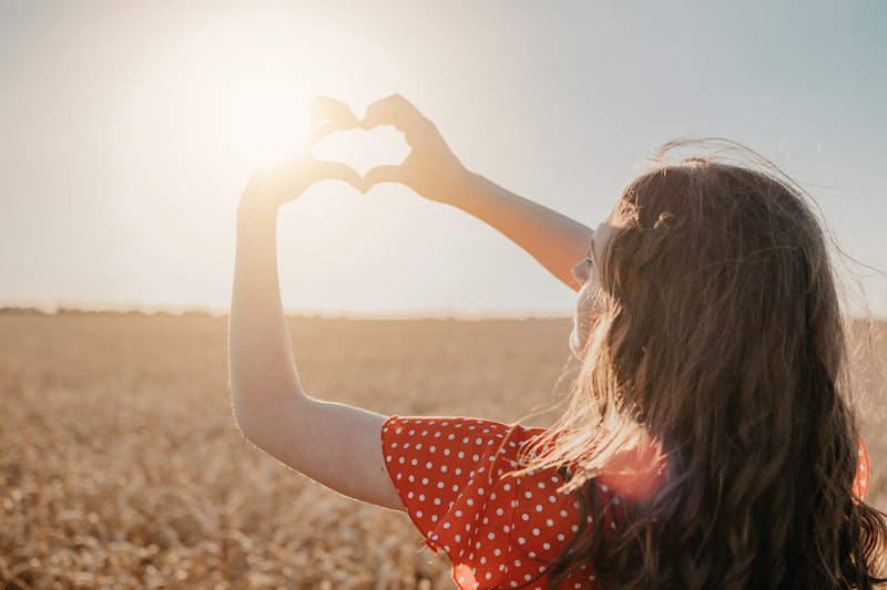 Frau macht mit Händen ein Herz vor der Sonne