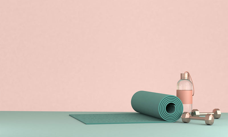 Eine Yogamatte, Sportflasche und kleine Kurzhanteln vor einem rosa Hintergrund