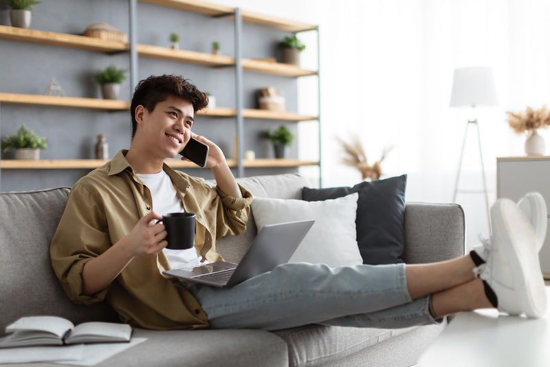 Mann sitzt mit Laptop auf Sofa und telefoniert