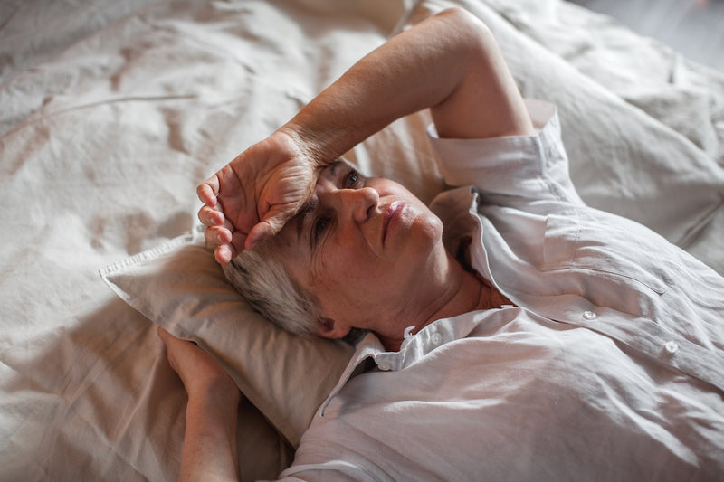 Frau liegt im Bett und legt sich den Arm an die Stirn