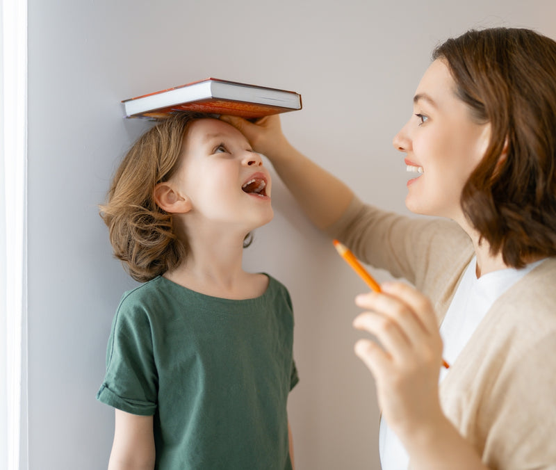 Mutter legt Buch zum Messen auf Kopf eines Kindes