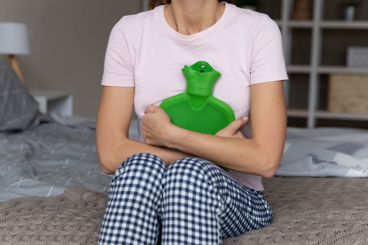 Frau hält sich eine Wärmflasche an den Bauch