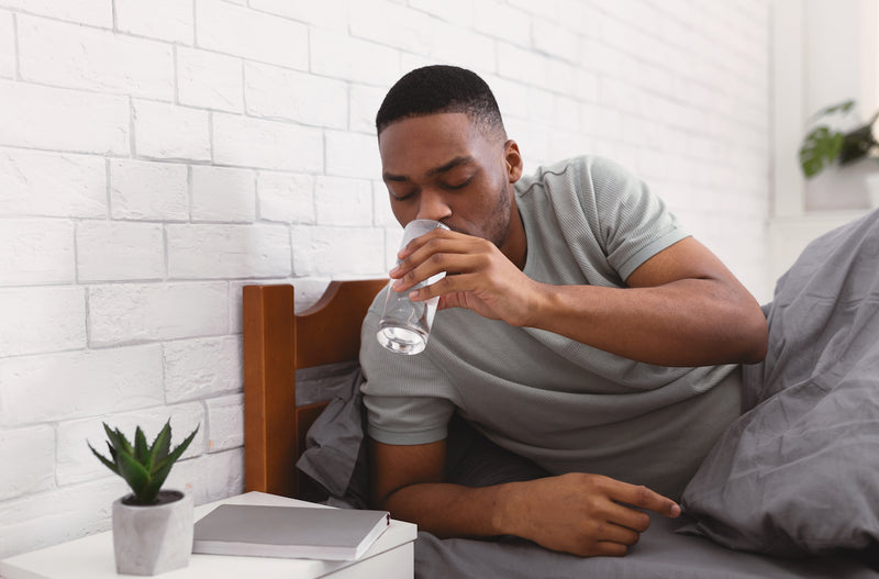 Man trinkt im Bett ein Glas Wasser