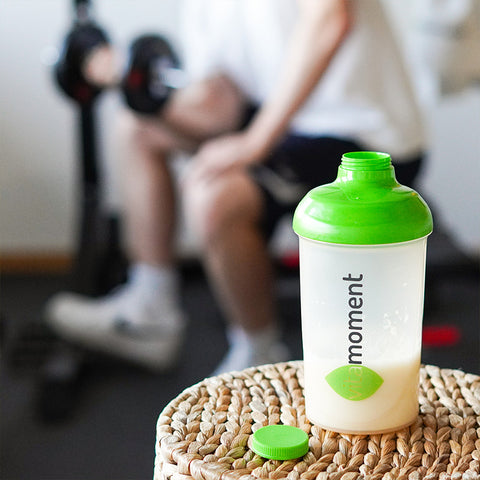 Auf einem Tisch in einem Fitnesstudio steht ein Eiweißshaker von VitaMoment