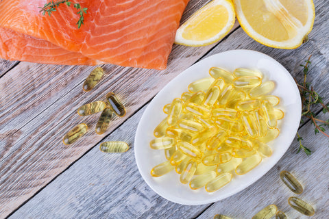 Fischöl vs. Algenöl: Ein Stück Lachs und ein Teller mit Fischöl-Kapseln