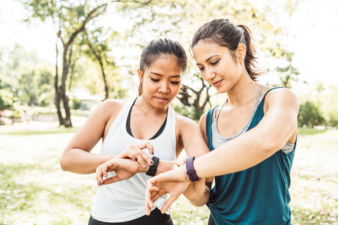 Fitness-Tracker Gesundheit: Zwei Frauen in Sportkleidung vergleichen die Ergebnisse auf ihren Fitnessuhren miteinander