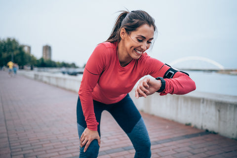 Fitness-Tracker Gesundheit: Frau in Sportkleidung schaut lächelnd auf ihre Fitnessuhr