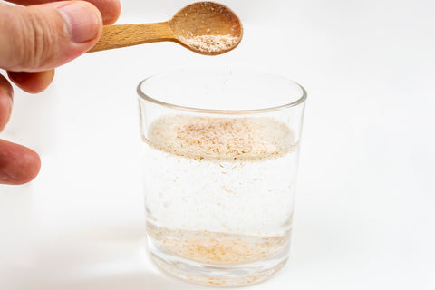 Flohsamen werden mit einem Löffel in ein Glas Wasser gegeben
