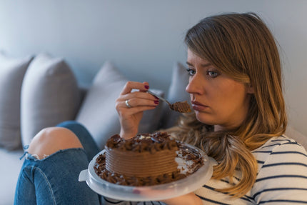 Abnehmen in den Wechseljahren: Frau sitzt traurig mit einer Schokotorte auf dem Sofa