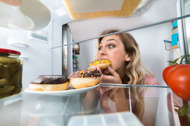 Frau isst Gebäck aus dem Kühlschrank