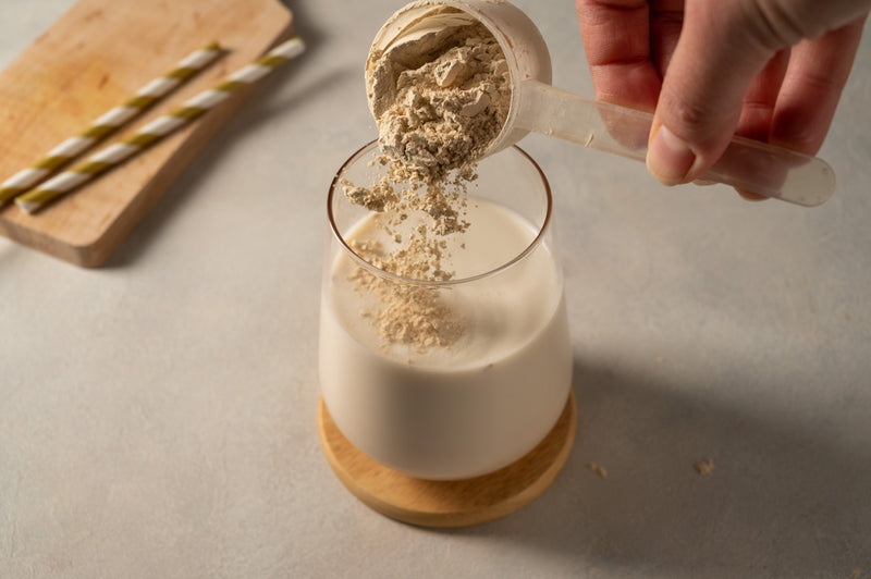 Proteinpulver wird in ein Glas mit Milch gegeben