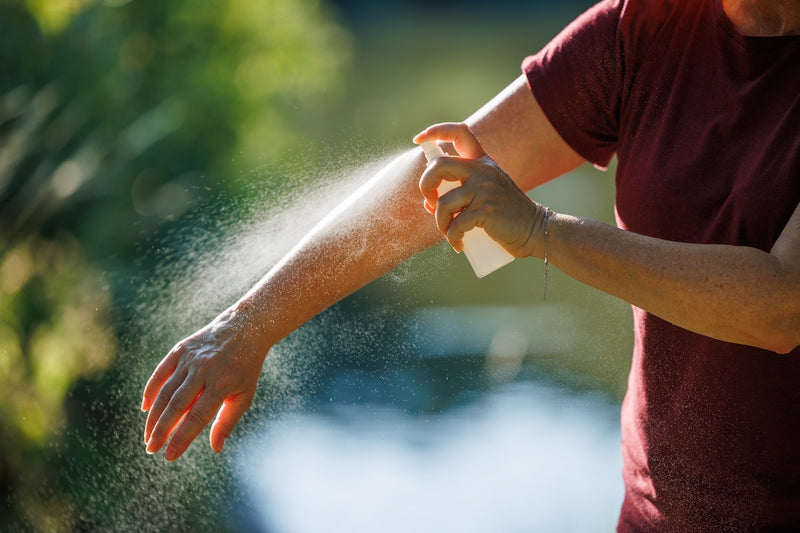 Mückenstiche behandeln: Person sprüht sich den Arm mit einem Mückenspray ein